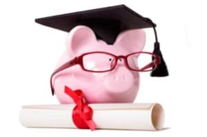 A pink piggy bank wearing glasses and a ceremonial graduation cap stands next to a diploma with a red tie.