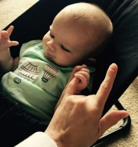 Baby holding mom's pinkie finger while mom signs "I love you" in ASL.