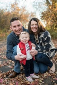 Mom, dad, and baby smiling together outside in fall