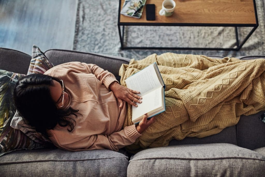 woman reading under a blanket on the couch: Top Ten Most Read Posts 2021