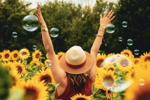 Woman standing in sunflower field facing away from the camera with hands raised in the air.