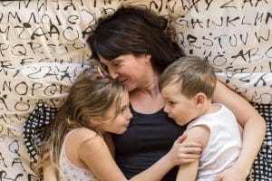 brunette mom snuggling toddler son and daughter in bed