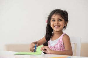 little girl cutting paper at a table