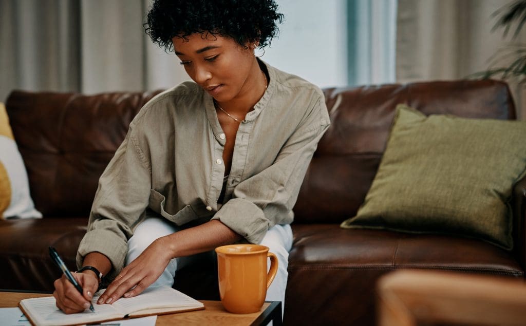 Cropped shot of a beautiful young woman writing in her notebook while sitting at home- Choosing a growth mindset