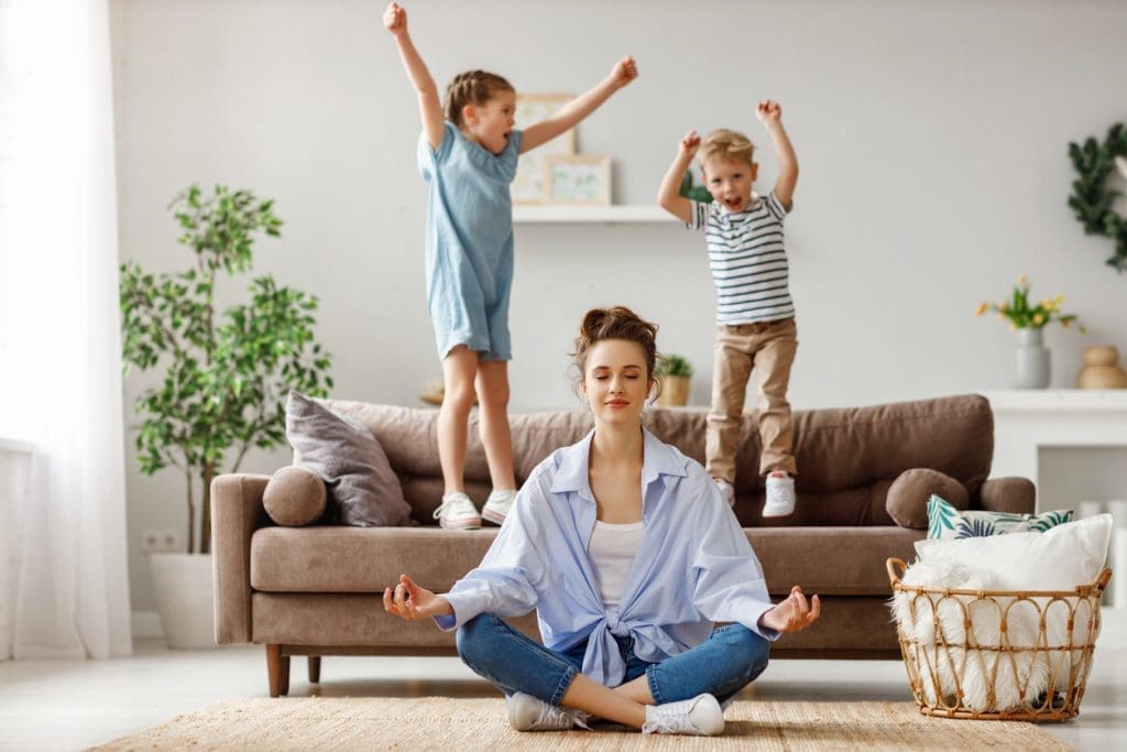 Mom practicing meditation while kids jump on couch - parenting battles not worth fighting