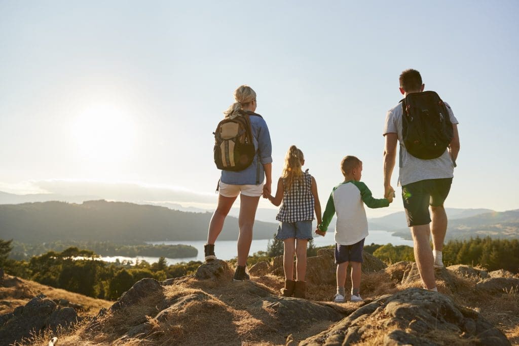 Travel with kids - rear view of mother, father and two children at the top of a hill overlooking a lake