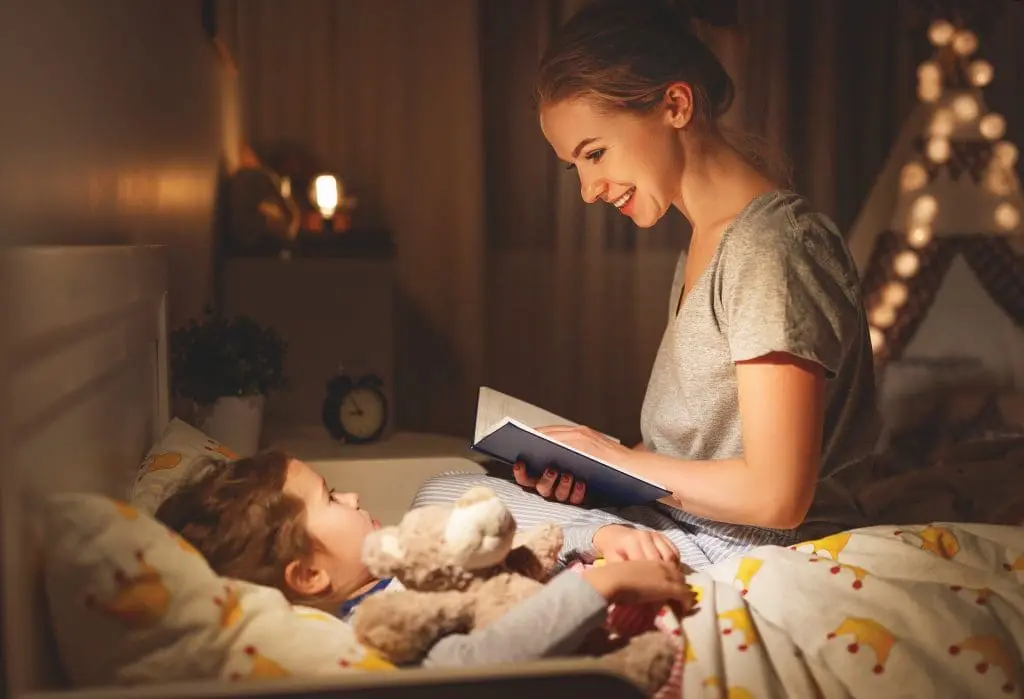Children Health and Wellness. mother and child daughter reading book in bed before going to sleep