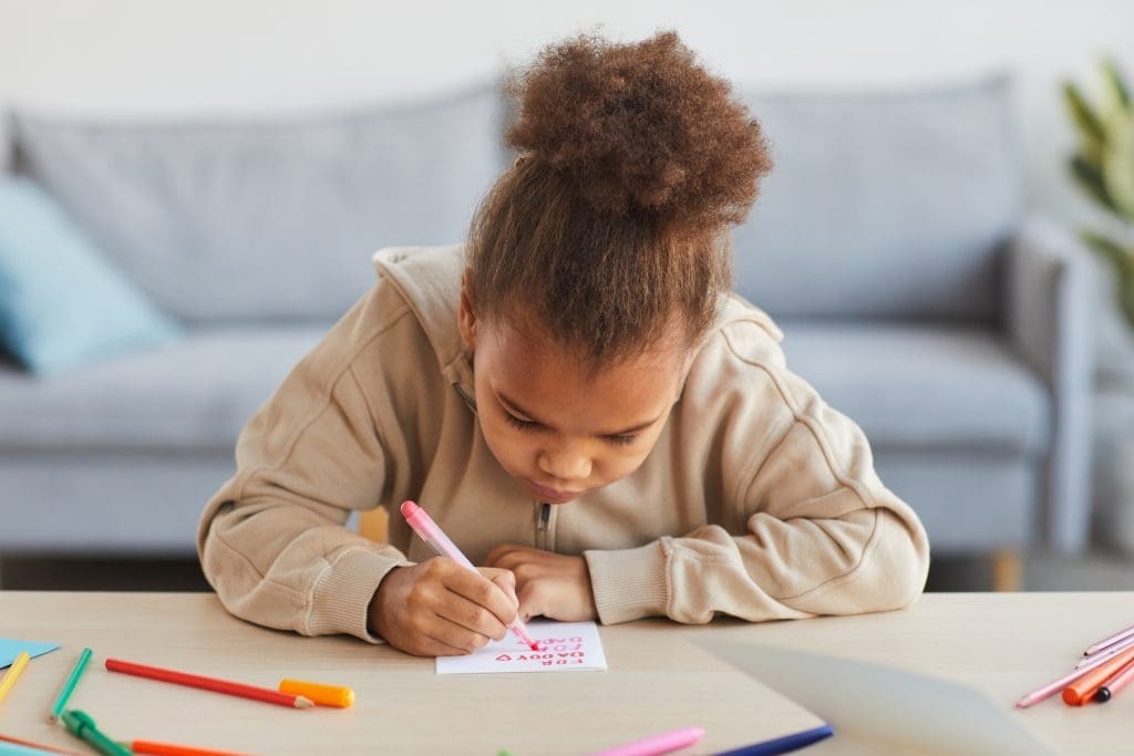 Front view portrait of cute African-American girl signing handmade card as gift for Fathers day, copy space