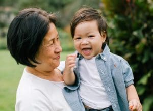Asian grandmother in white blouse holding and smiling at her toddler grandson
