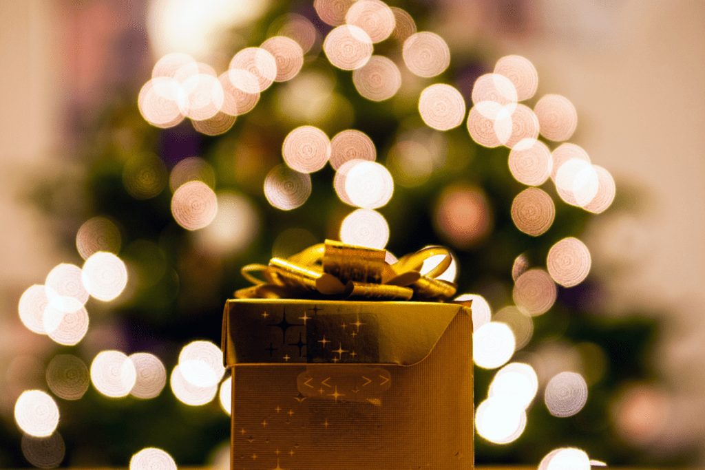 a gold wrapped present with a large bow in front of a christmas tree with blurred lights