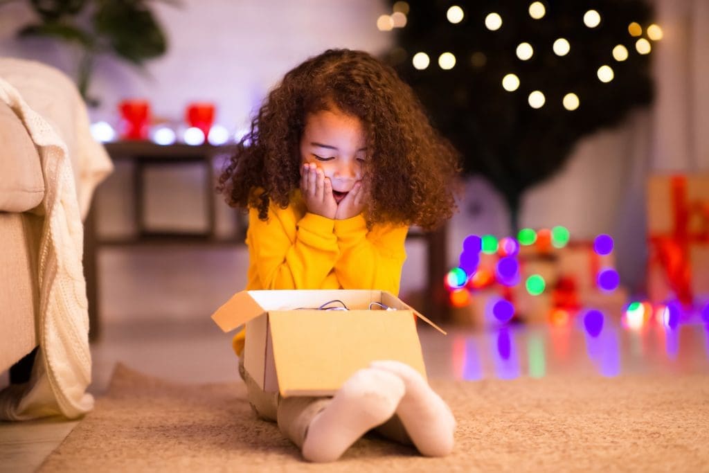 Experience gifts.A Shocked happy african american little girl enjoying Christmas gift near Xmas tree