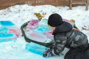 child in winter gear playing with colorful ice blocks outdoors