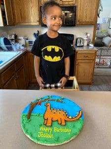 little boy standing in front of his dinosaur birthday cake