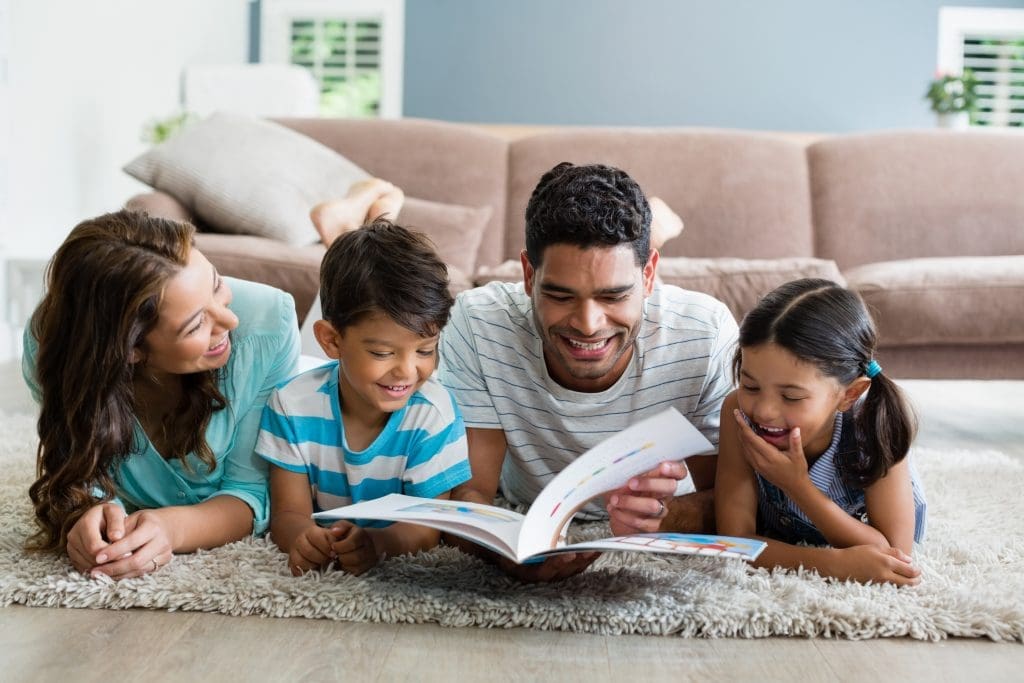 Parents and children lying on rug and reading book in living room at home - read across america day 2022