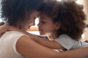 Close up head shot side view calm happy mixed race mother cuddling little cute daughter, touching foreheads.