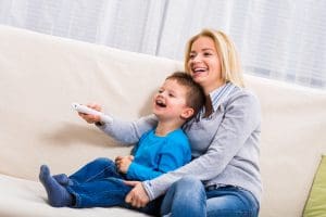 Happy mother and son are sitting on sofa and watching tv together. - Bluey