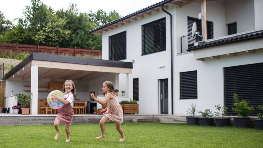 Summer Checklist - Two happy small girls sisters playing with a ball outdoors in the backyard, running.