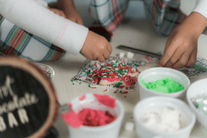 children sitting around a christmas cookie covered in red frosting with red, green, and white sprinkles